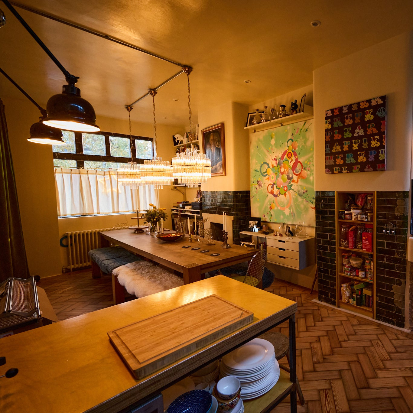 Modern kitchen with wooden countertops, pendant lights, and a colorful wall tapestry.